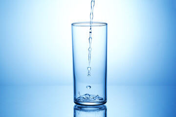 Pouring water into glass at mirror table against light blue gradient background, closeup