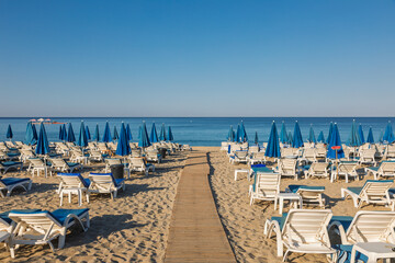 Early morning empty beach with loungers and blue umbrellas
