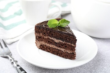 Piece of delicious chocolate cake with mint and fork on grey table, closeup