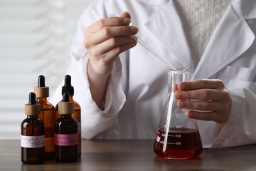 Professional perfumer developing luxury perfume at wooden table in laboratory, closeup