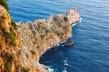 Tourist excursion boat exploring coastal sea caves near steep rocky cliffs in Mediterranean Turkey