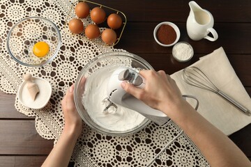 Woman whisking cream with hand mixer at wooden table, top view