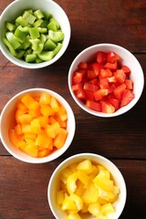 Pieces of fresh colorful bell peppers in bowls on wooden table, flat lay