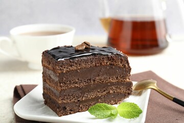 Piece of chocolate cake served with mint, spoon and tea on table, closeup