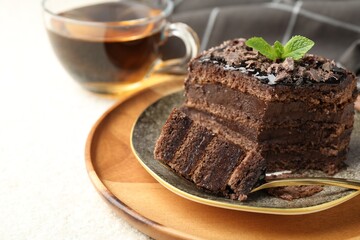 Piece of delicious chocolate cake with mint and tea on white table, closeup. Space for text
