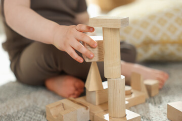 Cute little child playing with wooden building blocks at home, closeup