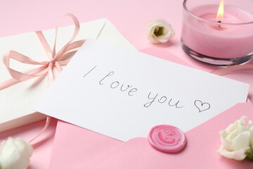 Stack of letters, card with phrase I Love You, burning candle and flowers on pink background,...