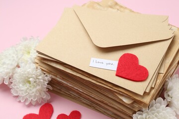 Stack of letters with phrase I Love You, flowers and red hearts on pink background, above view