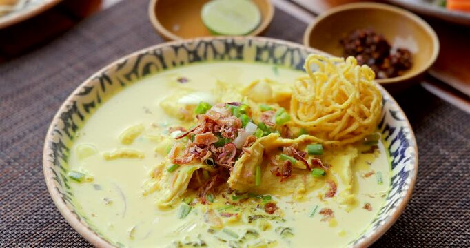 Thai Khao Soi curry noodles in decorative bowl. Authentic Chiang Mai cuisine garnished with shallots and lime on rustic mat. Asian food concept, spicy soup.
