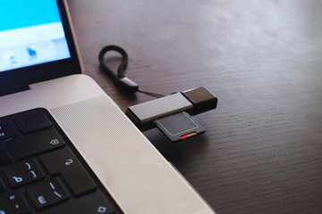 SD card Storage drive connected to a laptop with a USB card reader connector on a wooden desk.