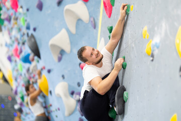 Man climbing a tall, indoor, man-made rock climbing wall