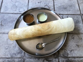 Indian masala dosa served with sambhar and chutney on a round metal plate.