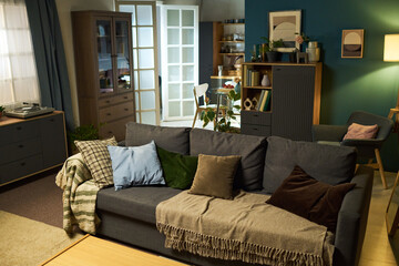 Empty modern living room with gray sofa and assorted pillows standing in foreground, open doors revealing dining area in background, no people present in scene