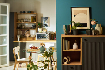 Modern kitchen and dining area featuring glass table with chairs, wooden shelves holding dishes and appliances, decorative plants and framed artwork on blue accent wall