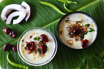 Two bowls of spicy coconut chutney, styled with coconut slices, green chilies, and curry leaves as props
