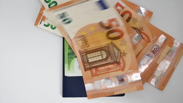 billetes de euros cayendo sobre un pasaporte en fondo blanco