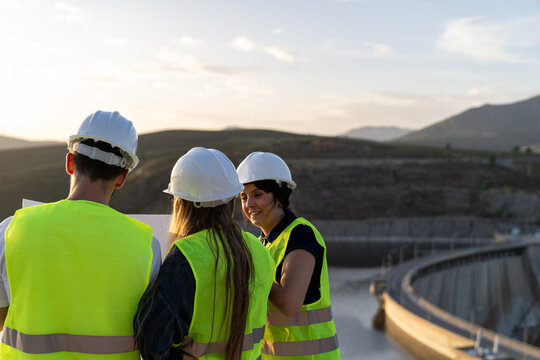 Engineers reading blueprint overlooking dam at sunset