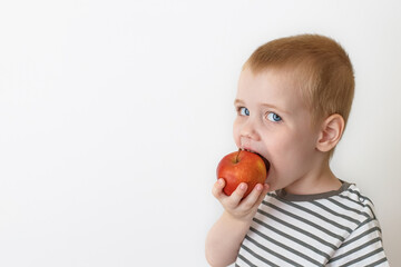 A cute child eats a red apple. The concept of healthy eating.