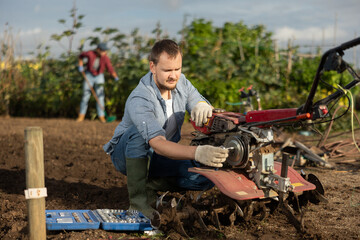 Farmer repairs a cultivator to work with the land. Man checks the work of garden equipment with tools © JackF