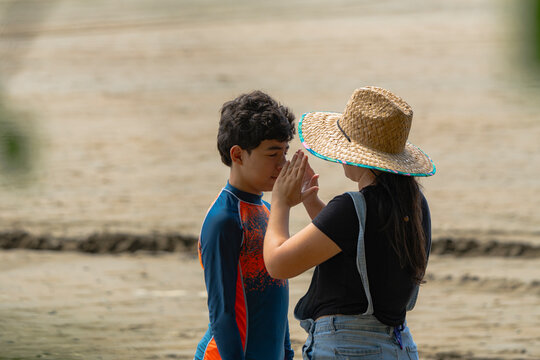 Latina mother applying sunscreen to teenage son on the beach - Powered by Adobe