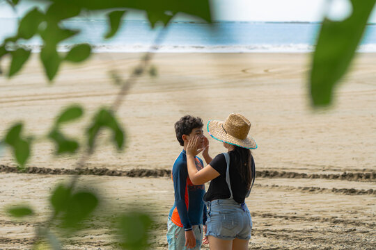 Latina mother applying sunscreen to teenage son on tropical beach