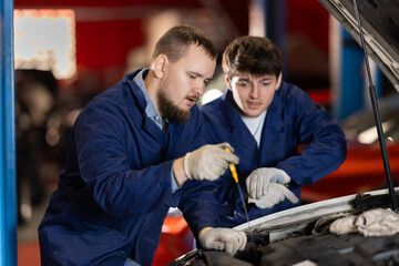 Two auto mechanics checking engine oil level under the hood of car together in a garage