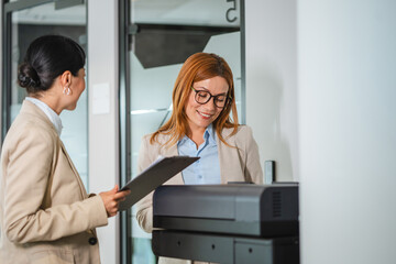 two multicultural female colleague stand in office by the copy machine