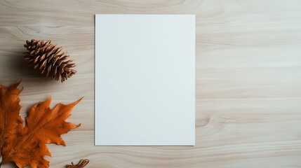 A blank white sheet of paper elegantly placed on a wooden surface, accompanied by autumn leaves and a pine cone, symbolizing creativity and the changing seasons.