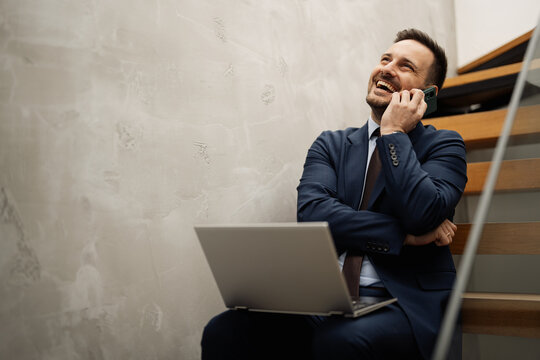 Businessman sitting on stairs and using laptop and smartphone