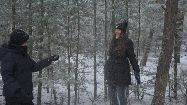 Mother and son on a winter walk in a snowy forest. The parent plays a fun prank, shaking a tree branch to create a surprise snow shower. The happy family is playing and laughing together outdoors.