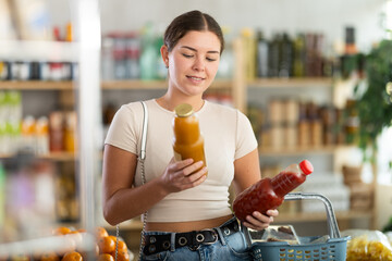 Girl hold packages bottles and choose consider juice in store. Market visitor choose consider make...