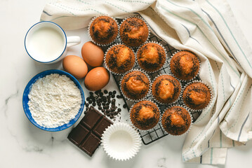 Top view of homemade chocolate muffins,chocolate,eggs,flour and a cup of milk