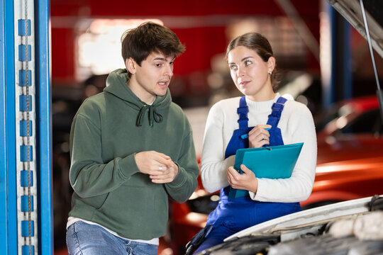 Client guy came to a car service to check car and receives advice from a female mechanic. Mechanic gives recommendations for the repair and replacement of parts by the car owner