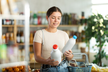 Girl hold packages bottles and choose consider milk in store. Market visitor choose consider make...