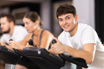 Obraz premium Young motivated guy training on an exercise bike in the gym
