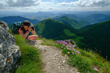 Young woman taking pictures of flowers in the mountains. Summer day in Mala Fatra mountain range in Slovakia