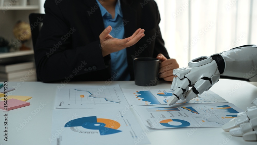 Poster a human and a robotic arm engage in a business discussion, analyzing charts and data reports on a de