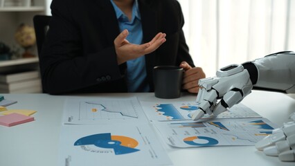 A human and a robotic arm engage in a business discussion, analyzing charts and data reports on a...