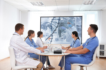 Team of doctors using video projector during conference about DNA indoors. Illustrations on projection screen