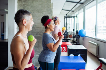Senior women lifting dumbbells during group fitness class at gym