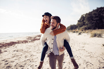 Playful couple piggyback riding on the beach during autumn vacation