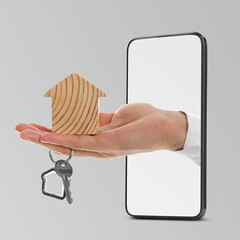 Man's hand with house figure and key sticking out from smartphone on grey background. Real estate...