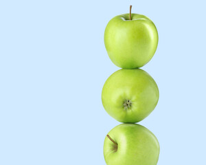 Green apples stacked on top of each other against light blue background. Balance