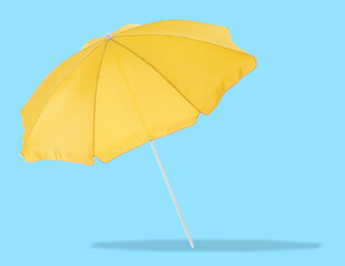 Yellow beach umbrella casting shadow on light blue background