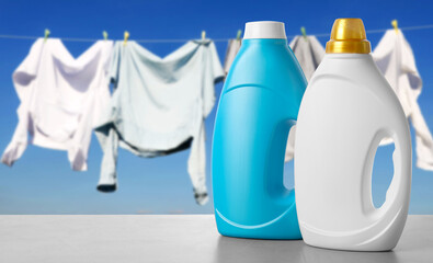 Fabric softener and laundry detergent on table outdoors, space for text. Clothes drying against sky