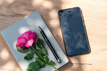 Smartphone with pink rose and pen on desk with notebook, minimal and calm work setup