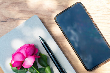 Pink rose and pen with smartphone in natural light on desk, peaceful work from home morning