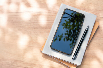 Smartphone on notebook under leaf shadows, pen on side — calm workspace