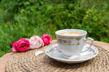 A cup of coffee with a pink rose on a rustic table, representing relaxation and cozy morning vibes.