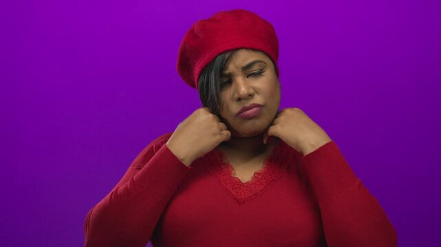 Woman wearing red beret with closed eyes adjusting her sweater on a vibrant purple background emphasizes mood and style.